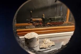 Hinter einem runden Guckloch steht eine Modelleisenbahn (um 1850) und ein Betonbohrkern