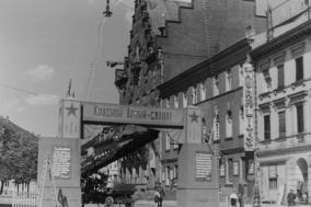 Die Überblendung reicht von dem historischen Foto von 1945 bis 2021. Auf dem Foto vom Mai 1945 steht vor dem Gebäude ein Triumphbogen aus Holz.