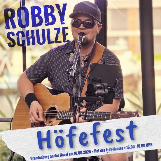 Plakat für das Konzert von Robby Schulze: der Künstler steht mit seiner Gitarre am Mikrofon, trägt Basecap und Sonnenbrille. Er ist etwa 40 Jahre alt.